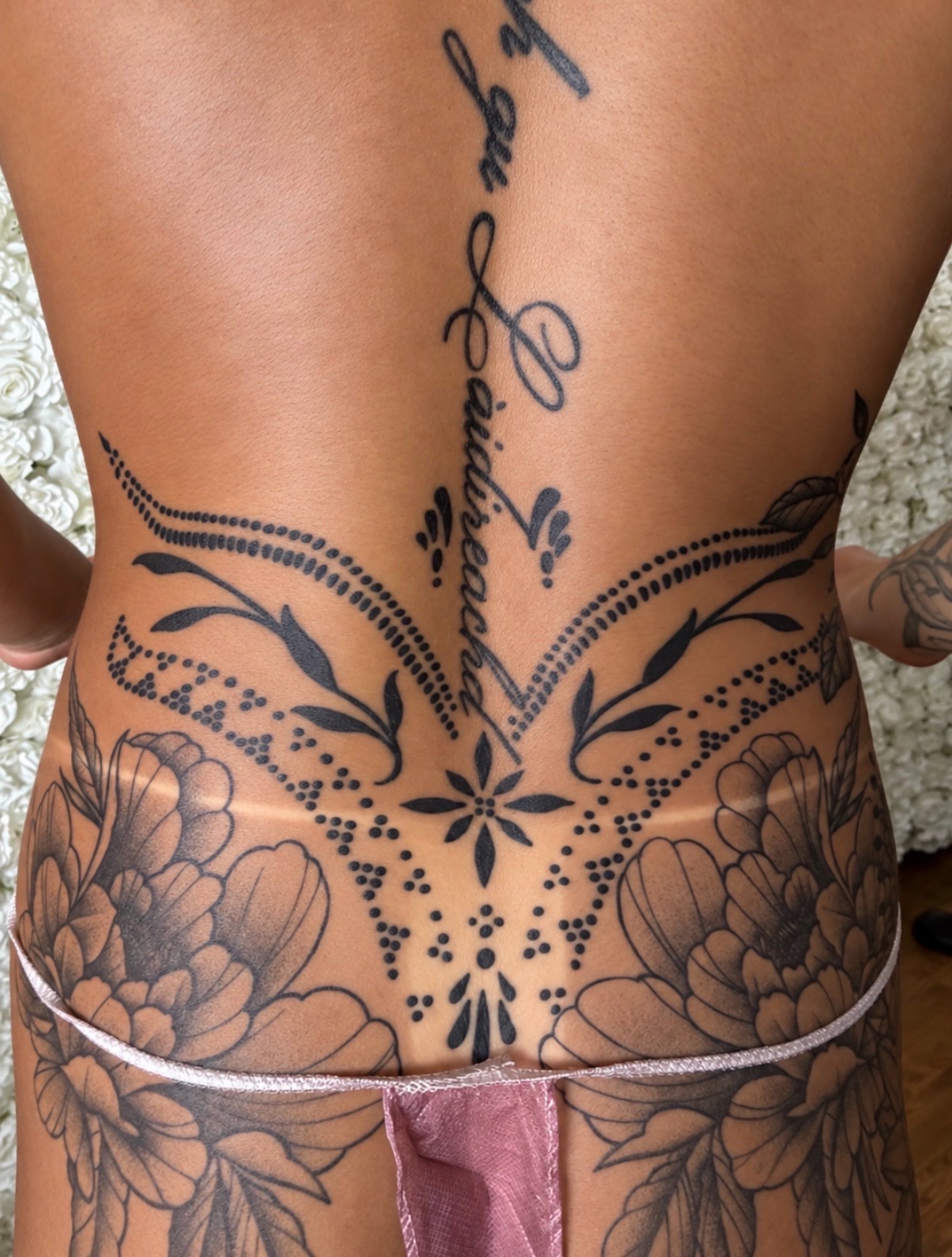 Deep, even bronze spray tan across a tattooed lower back with crisp, clean tan lines