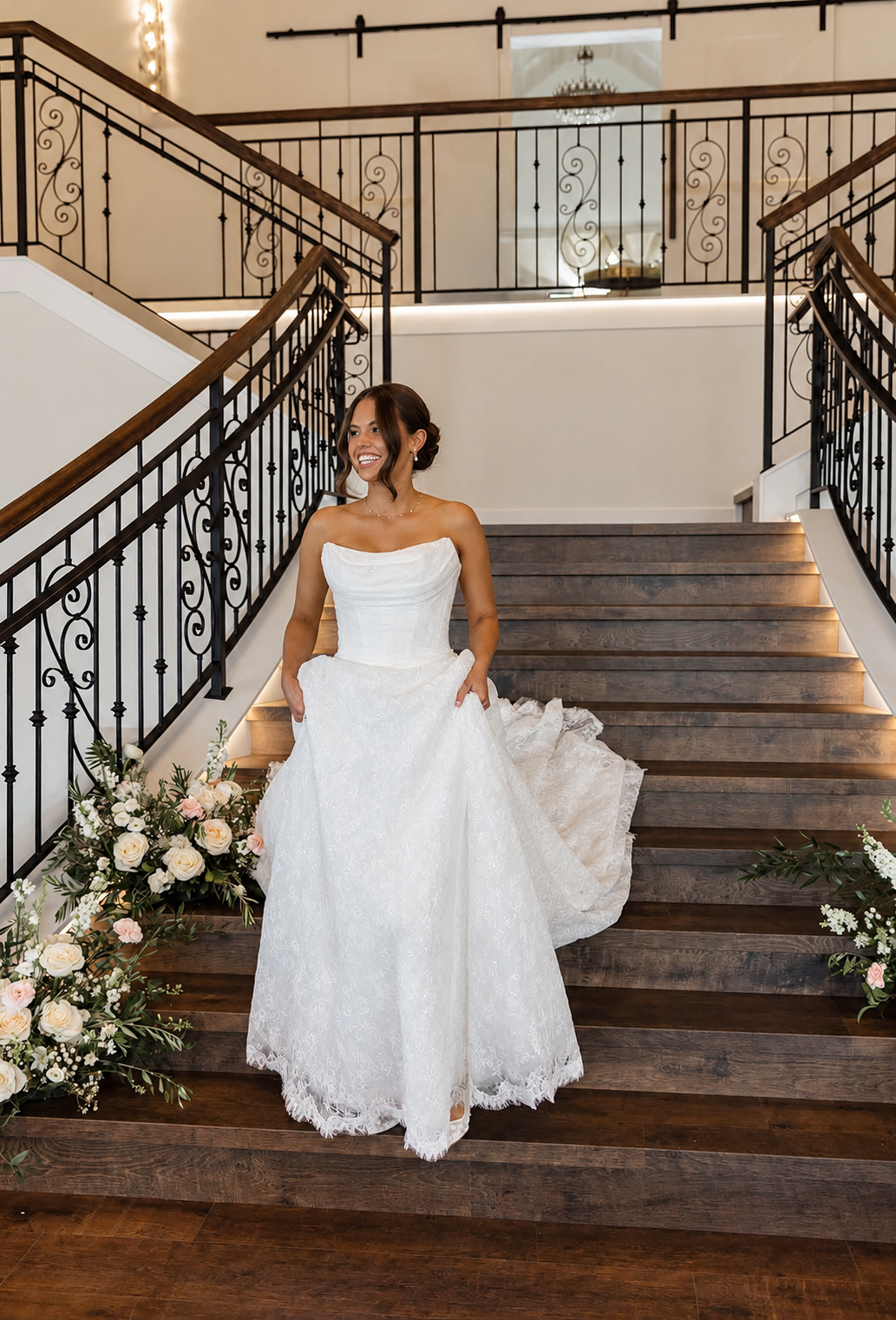 Bride in a strapless white lace gown descending a grand staircase with a natural sun-kissed bridal glow