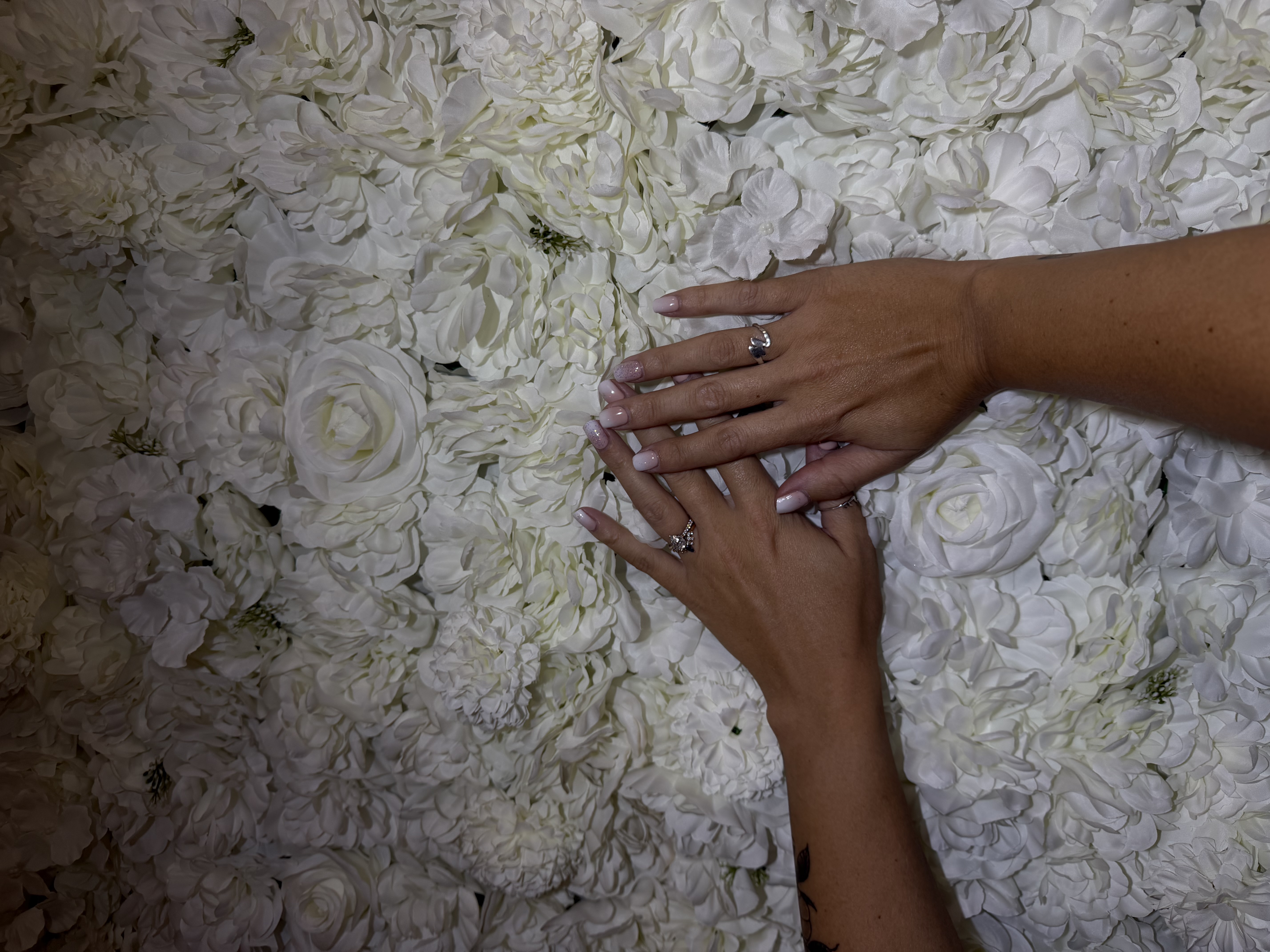 Two sun-kissed hands with soft pink ombre nails resting on a white floral wall