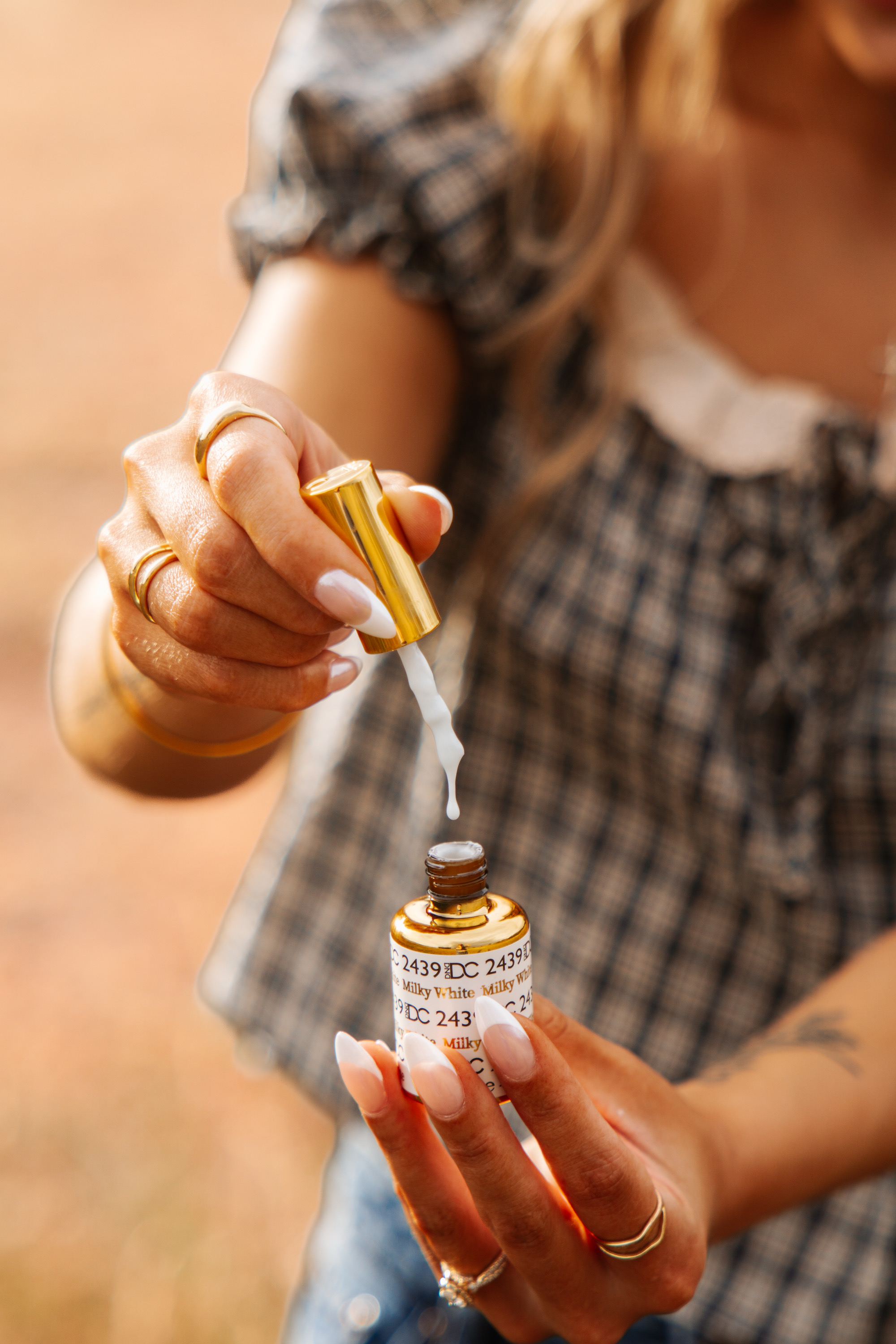 Close-up branding shot of freshly manicured French-tip almond nails and a sun-kissed glow, holding a gel polish bottle at golden hour