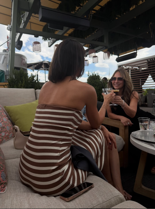 Two friends with sun-kissed tans enjoying cocktails on a rooftop patio at golden hour